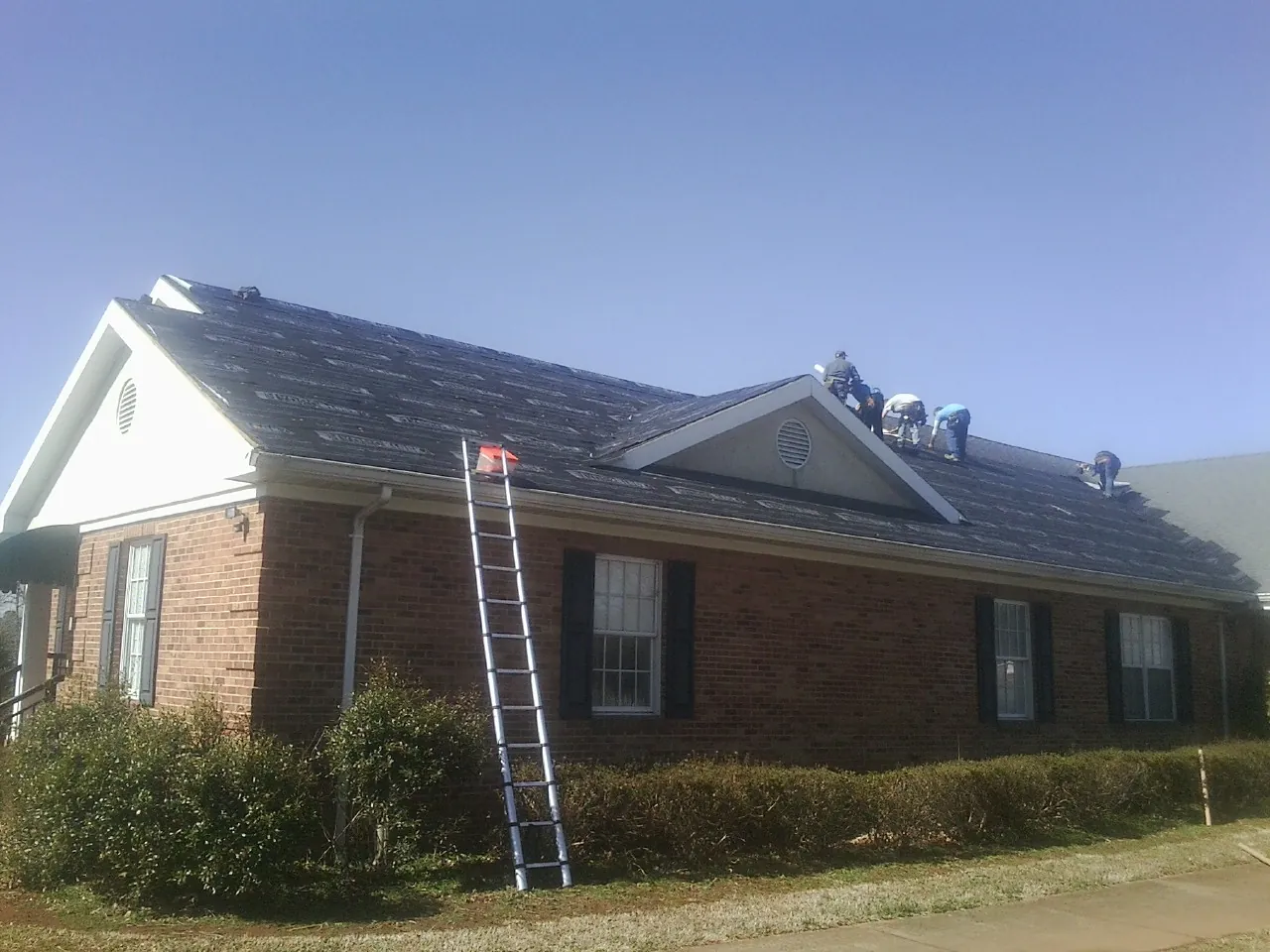 Crew tearing shingles off a brick ranch roof with a ladder set — Emergency Roof Repair work by our crew in Manville