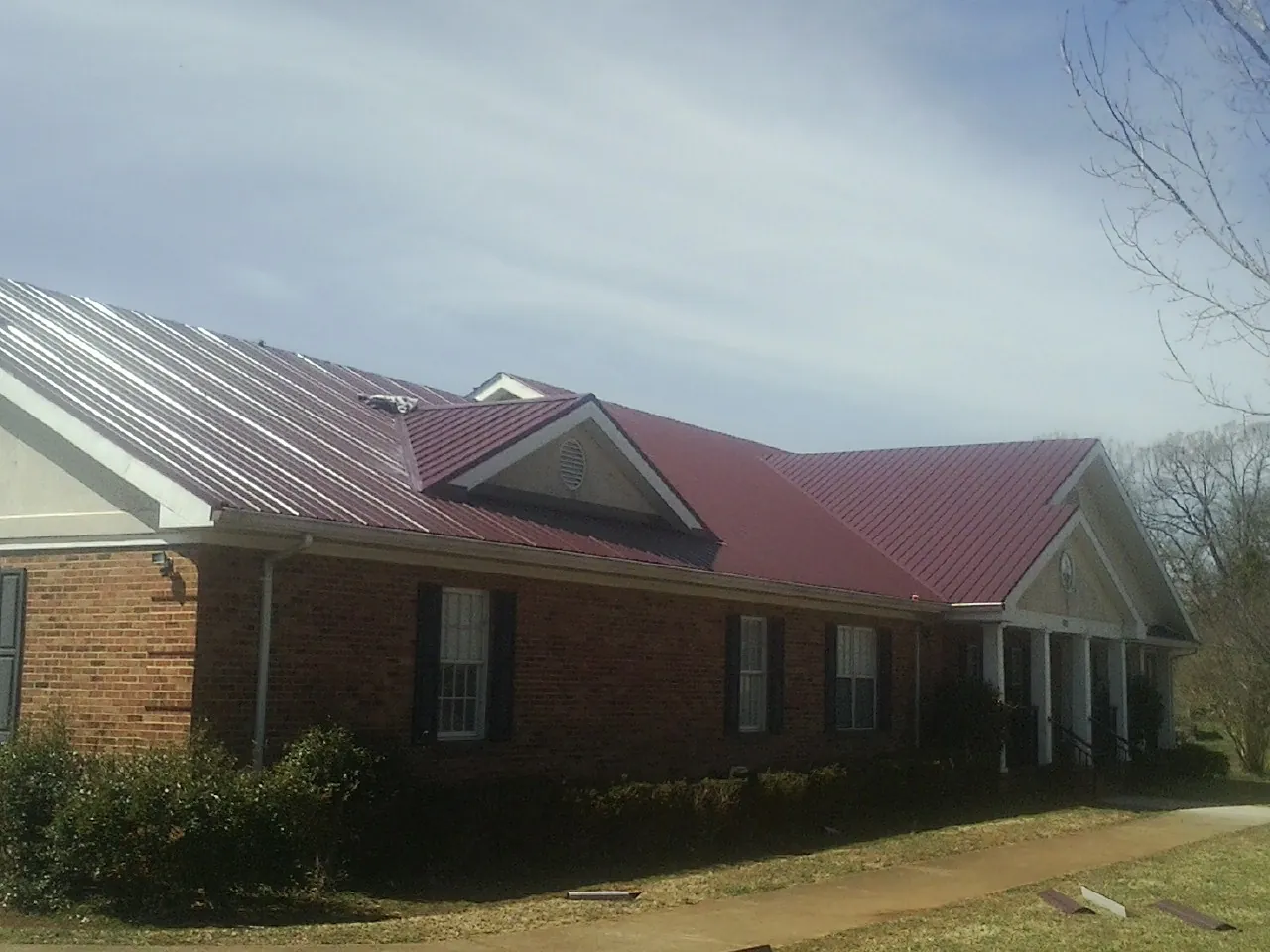 Red metal roof with gabled entries on a long brick building, from a Hail Damage Roof Repair job in Manville