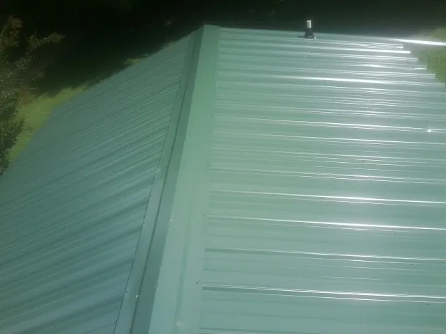 New green metal panels meeting at the ridge of a roof — Flat Roof Repair work by our crew in Manville